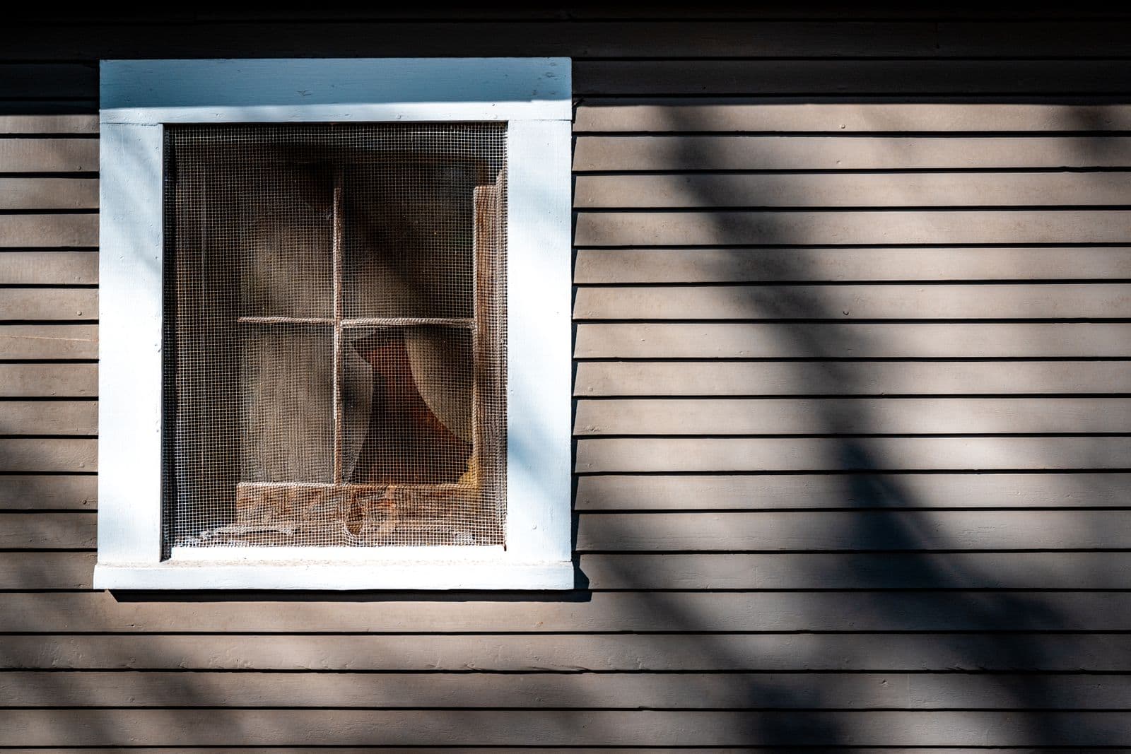 Window set in dark horizontal siding, striped by shadows