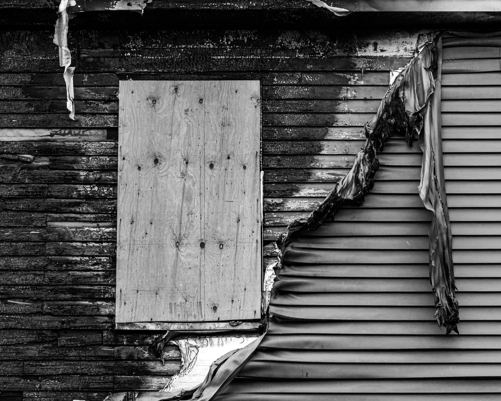 Black and white view of damaged siding pulling away from a wall
