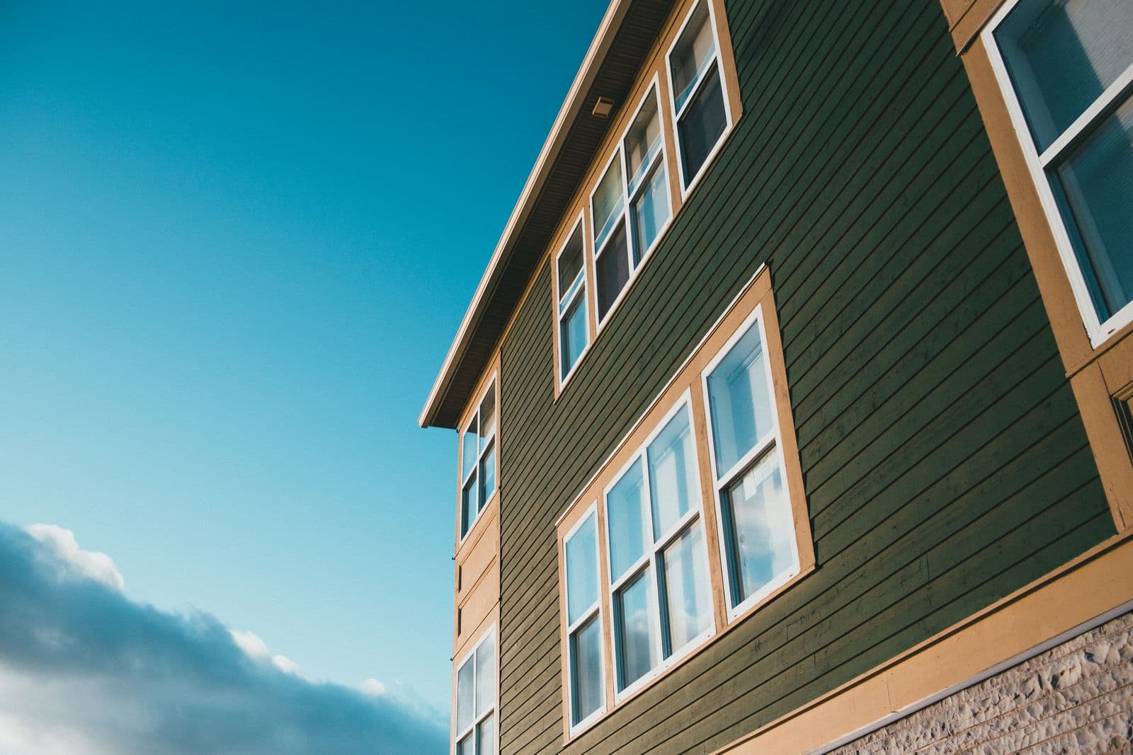 Green wooden house with white window frames under a clear sky